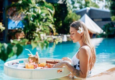 Female tourist in luxurious hotel enjoys swimming pool and tropical food